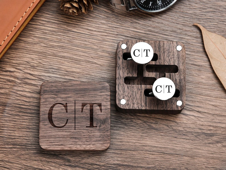 May include: A wooden box with two cufflinks inside. The cufflinks are silver with the initials "C|T" engraved on them. The box is also engraved with the initials "C|T".