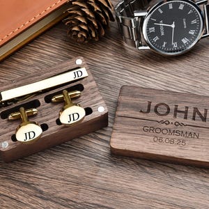 May include: A wooden box with a gold tie clip and cufflinks. The box is engraved with the name "JOHN" and the words "GROOMSMAN" and the date "06.08.25".