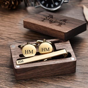 May include: A wooden box with a personalized engraved name "Michael" on the lid. The box contains a gold tie clip and two gold cufflinks with the initials "HM" engraved on them.