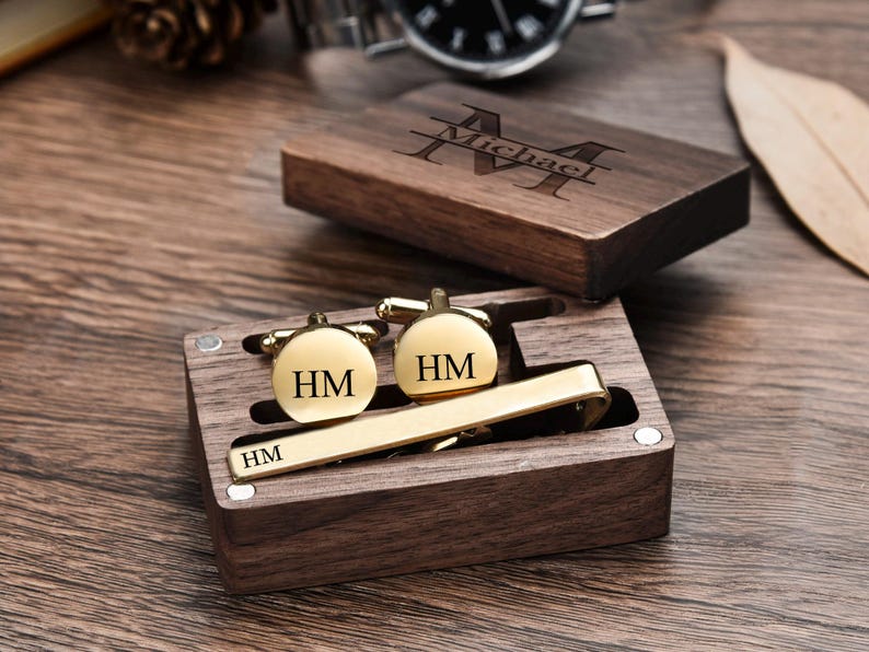 May include: A wooden box with a personalized engraved name "Michael" on the lid. The box contains a gold tie clip and two gold cufflinks with the initials "HM" engraved on them.