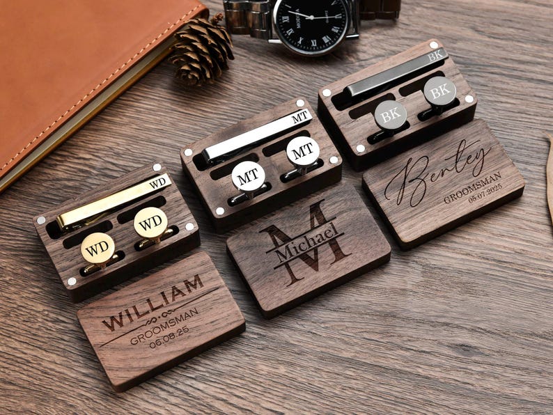 May include: Set of six wooden boxes with engraved names and dates. Each box contains a tie clip and cufflinks. The boxes are arranged on a wooden surface.