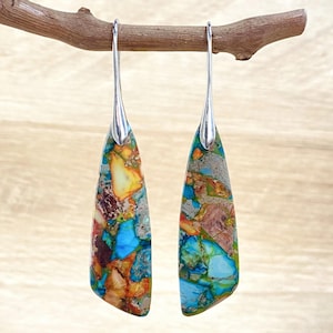 May include: A pair of silver dangle earrings with a teardrop-shaped stone. The stone is a mix of blue, green, orange, and brown colors.