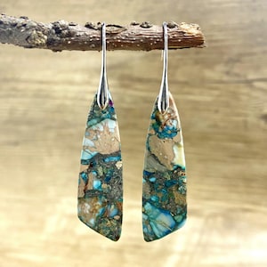 May include: A pair of silver dangle earrings with a teardrop-shaped stone. The stone is a mix of brown, blue, and white colors with a speckled pattern.