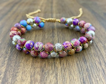 May include: A double-strand bracelet with colorful, speckled beads and silver accents. The bracelet is made with a knotted cord and has a sliding knot for adjusting the fit.