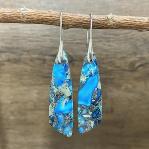 May include: A pair of dangle earrings with blue and grey marbled stone accents. The earrings are silver and have a teardrop shape.