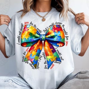 May include: White t-shirt featuring a colorful puzzle piece bow design. The bow is composed of various colors, including blue, yellow, red, and green. Text around the bow reads "I would not change the world for you, but I would change the world for you."