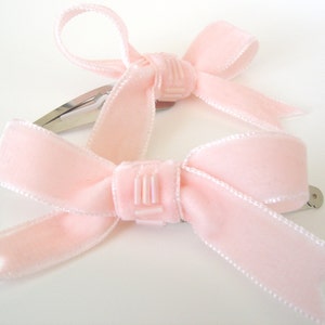 Puede incluir: Dos pinzas para el pelo de terciopelo rosa con dise&ntilde;o de lazo. Cada pinza tiene una barra de metal plateado.