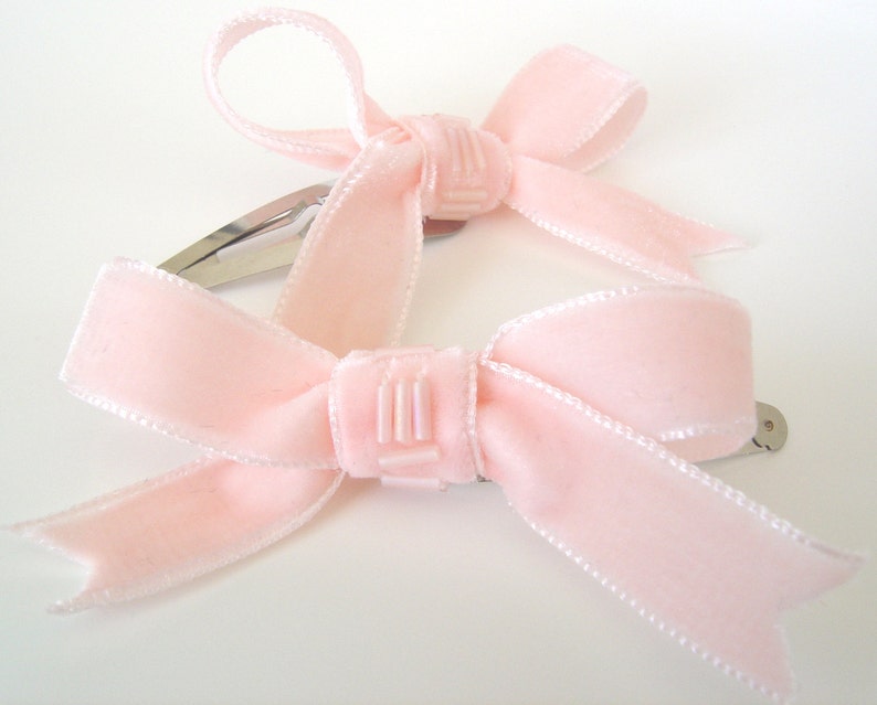 Puede incluir: Dos pinzas para el pelo de terciopelo rosa con dise&ntilde;o de lazo. Cada pinza tiene una barra de metal plateado.