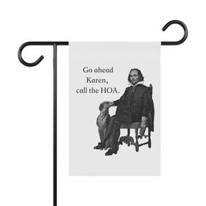 Puede incluir: Una bandera de jardín blanca con un soporte de metal negro. La bandera presenta una ilustración en blanco y negro de un hombre y un perro, con el texto "Go ahead Karen, call the HOA."