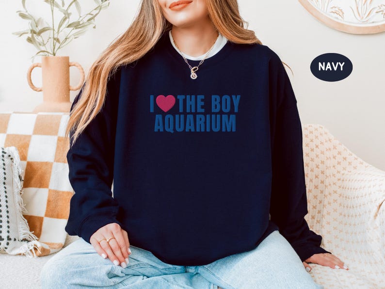 May include: Navy blue sweatshirt with the text "I ❤ THE BOY AQUARIUM" in blue, with a pink heart. The sweatshirt is a crew neck style. The word "NAVY" is in a navy blue circle in the upper right corner.