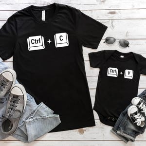 May include: Two black t-shirts with white text and keyboard symbols. The larger shirt says "Ctrl + C" and the smaller shirt says "Ctrl + V".