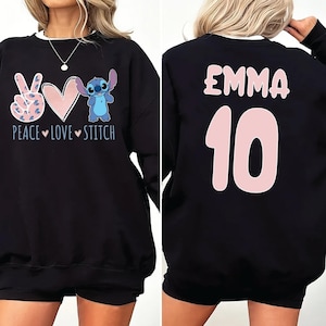 May include: Black sweatshirt with a peace sign, heart, and Stitch character on the front. The back of the sweatshirt has the name "EMMA" and the number "10" in pink.