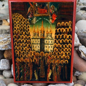 May include: A religious icon with a red frame, displaying a detailed painting. The artwork shows many figures, angels, and a central building with golden spires. The style is reminiscent of traditional religious art.