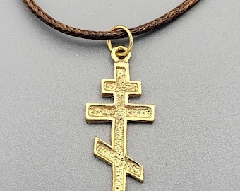 May include: A gold-colored pendant necklace with a cross pendant. The cross is a traditional Orthodox Christian cross with a slanted crossbar.