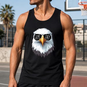 A man wearing a black tank top with a graphic of an eagle and the text "GAME DAY" stands in front of a basketball hoop.
