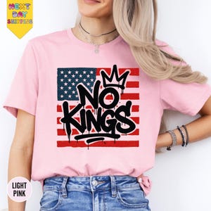 a woman wearing a pink shirt with the words no kings on it