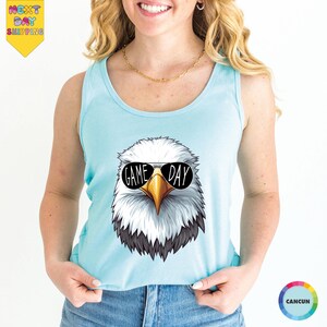 A woman wearing a light blue tank top with a graphic of an eagle wearing sunglasses and the text "GAME DAY" printed on it.
