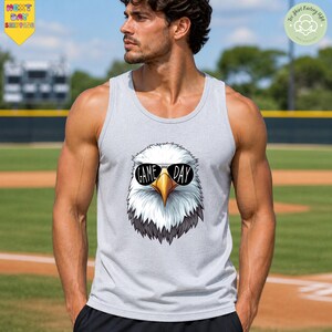 A man wearing a gray tank top with a graphic of an eagle wearing sunglasses and the text "GAME DAY" printed on it, standing on a baseball field.