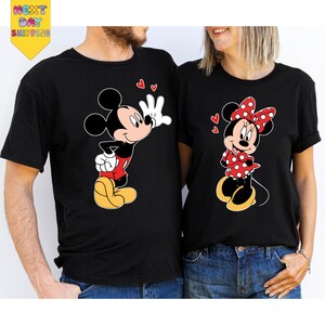 A man and a woman are standing next to each other, both wearing black t-shirts with Mickey Mouse designs.