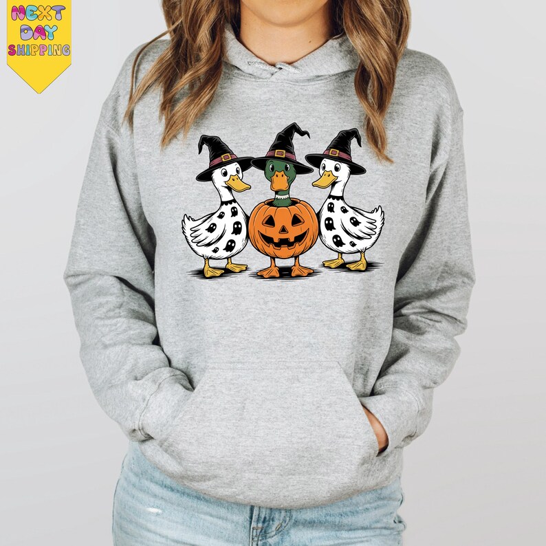 A gray hoodie with a Halloween-themed graphic design featuring three white ducks wearing witch hats and a carved pumpkin.