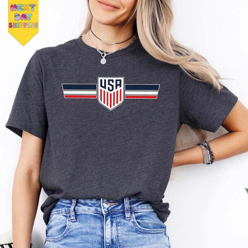 A woman wearing a gray t-shirt with a graphic of the United States flag and a necklace.