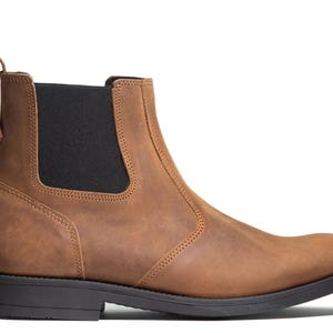 Pode incluir: Bota Chelsea de couro castanho com painel lateral el&aacute;stico preto e puxador. A bota tem sola preta e salto baixo. O couro tem um aspeto envelhecido.