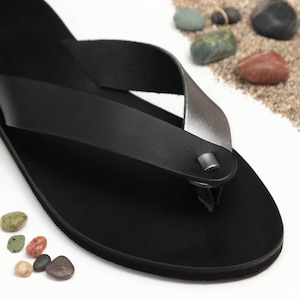 May include: Black leather thong sandals with a silver strap and a buckle closure.