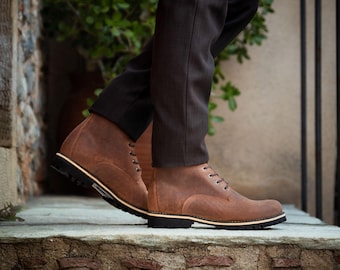May include: Brown leather lace-up boots with a thick sole. The boots are worn by a person standing on a stone step.