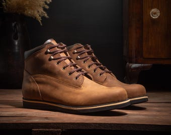 May include: A pair of brown leather boots with dark brown laces. The boots have a classic design with a sturdy sole and a padded collar. The boots are placed on a wooden surface, suggesting a rustic or outdoorsy theme.