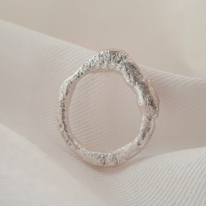Op de afbeelding: Een zilveren ring met een unieke, organische vorm. De ring is getextureerd en heeft een ruwe, onafgewerkte uitstraling.