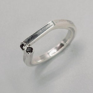 Puede incluir: Un anillo de plata con dos piedras preciosas negras engastadas en la banda.