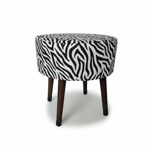 May include: A round ottoman with a zebra print fabric top and sides. The black and white pattern contrasts with the dark brown wooden legs. The stool has four legs and is set against a white background.