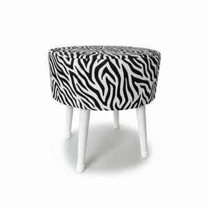 Könnte beinhalten: Ein runder Hocker mit einem Bezug aus schwarz-weißem Zebra-Print. Der Hocker hat vier weiße Holzbeine. Ein auffälliges Design für jeden Raum, ca. 40 cm Durchmesser.