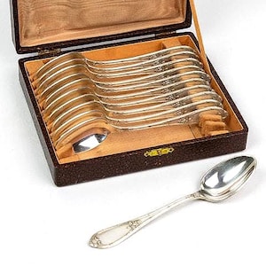 Peut inclure: Un ensemble de cuillères en argent dans un coffret en similicuir marron avec un intérieur marron clair. Les cuillères sont disposées soigneusement à l'intérieur de la boîte, avec une cuillère à l'extérieur. Les cuillères ont un motif floral décoratif.