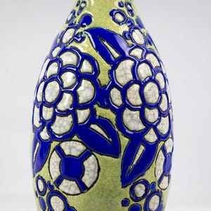 May include: A decorative ceramic vase with a bulbous shape. The vase features a light green background with a bold blue floral pattern. The flowers have a white, cracked texture, adding visual interest to the design.
