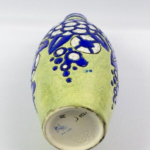 May include: A vintage ceramic vase with a light green background and blue floral designs. The vase has a textured surface and a round base. The bottom of the vase has markings including the number 892.