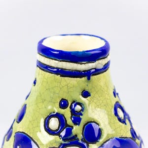 May include: A ceramic vase with a light green, cracked glaze. The vase features blue and white accents, including a blue rim and decorative blue circles. The interior is a cream color.