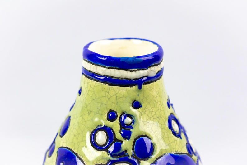 May include: A ceramic vase with a light green, cracked glaze. The vase features blue and white accents, including a blue rim and decorative blue circles. The interior is a cream color.