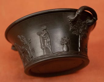 May include: Black ceramic bowl with two handles and a raised design of a woman holding flowers, a tree, and a vase of flowers.