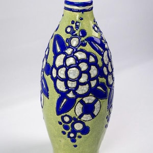 May include: A ceramic vase with a light green background and blue floral designs. The vase has a bulbous shape with a narrow neck and a blue rim. The floral pattern includes large flowers and smaller circular accents.