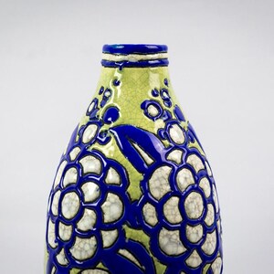 May include: A ceramic vase with a unique floral design. The vase features a light green background with a blue floral pattern. The flowers have a white center and a blue outline. The top and rim of the vase are blue.