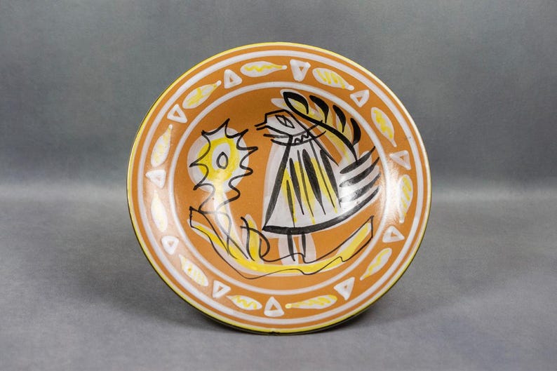 Vue de face de la coupe sur pied en faïence émaillée signée Jos Le Corre, décor stylisé d’un oiseau sur fond ocre