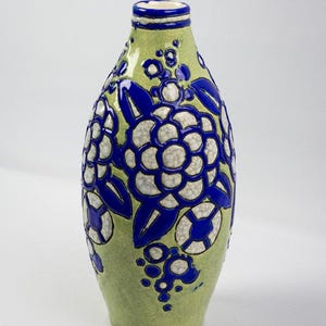 May include: A green ceramic vase with a floral design. The vase has a rounded body and a narrow neck. The floral pattern is white and blue, with the flowers and leaves outlined in blue. The vase is approximately 10 inches tall.