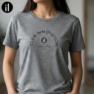 May include: A heather gray t-shirt with a crew neck. The shirt features a circular design with the words "CLUB INNOVATION" and "Members Only" printed in a dark gray color. The design also includes the letters "il" and the year "2023".