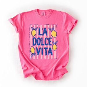 A pink t-shirt with a graphic design featuring the text "L'A DOLCE VITA" and lemon illustrations.