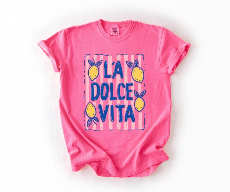 A pink t-shirt with a graphic design featuring the text "L'A DOLCE VITA" and lemon illustrations.