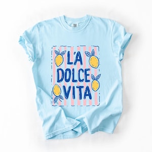A light blue t-shirt with a graphic design featuring the text "LA Dolce Vita" surrounded by lemon and lime illustrations.