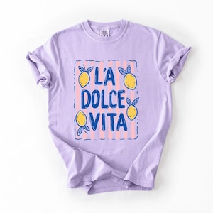 A purple t-shirt with a graphic design featuring the text "LA Dolce Vita" surrounded by lemon and lime illustrations.