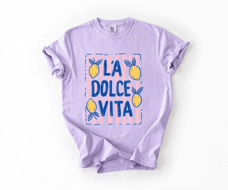 A purple t-shirt with a graphic design featuring the text "LA Dolce Vita" surrounded by lemon and lime illustrations.