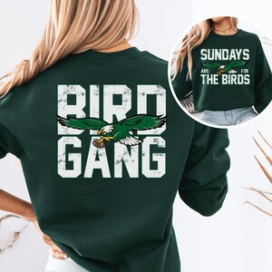 a woman wearing a green sweatshirt with the words bird gang on it